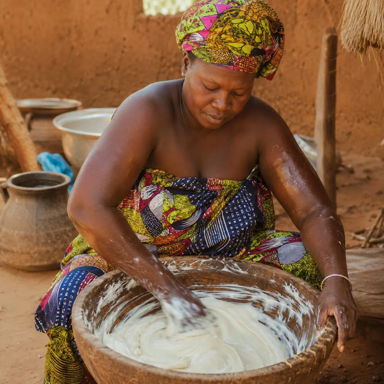 Femme barattant le beurre de karité brut à la main dans un grand bol — geste ancestral camerounais